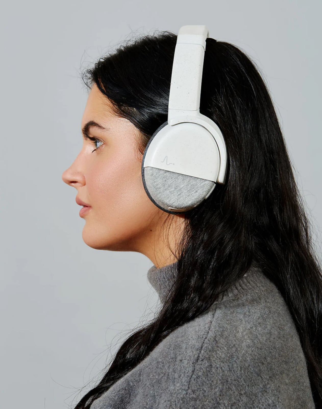 A side portrait photo of a young woman wearing Neurable’s Enten smart headphones in white colourway.